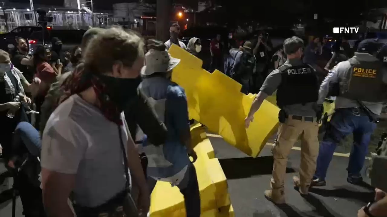 Policías y agentes federales frente al centro ICE mientras manifestantes gritan consignas.