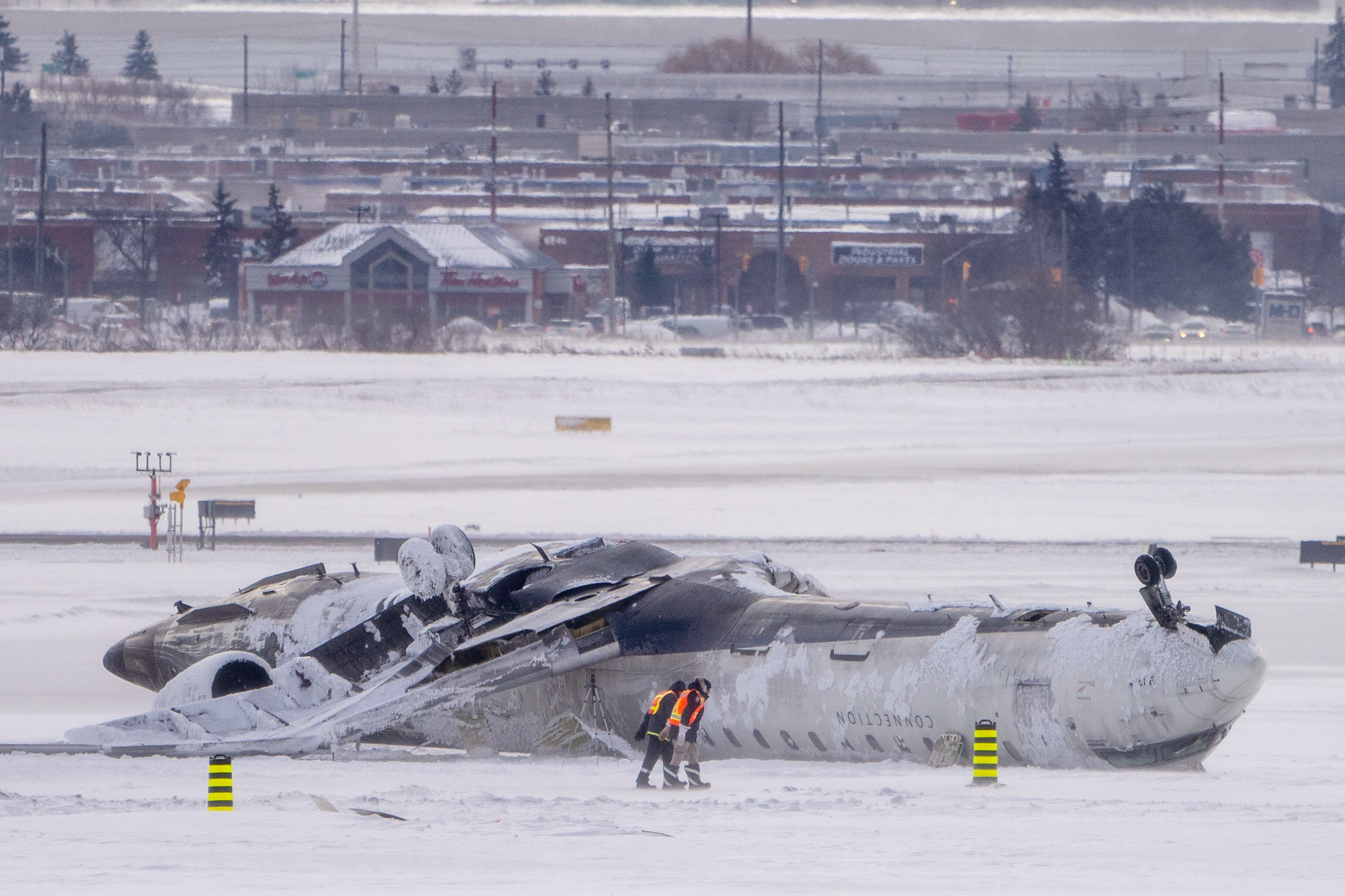 Trabajadores aeroportuarios inspeccionan el lugar del accidente aéreo de Delta Air Lines, que dejó al menos 18 pasajeros heridos, en el Aeropuerto Internacional Pearson de Toronto el 18 de febrero de 2025 en Toronto