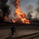 Archivo - Un hombre en su bicicleta pasa cerca de flamas y humo tras un incendio ocasionado por un ataque ruso en Járkiv, Ucrania, el 25 de marzo de 2022.