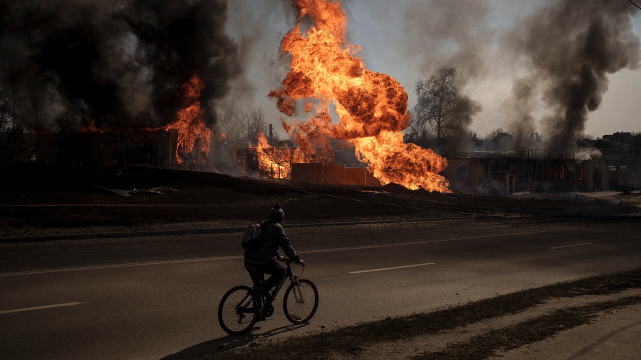 Archivo - Un hombre en su bicicleta pasa cerca de flamas y humo tras un incendio ocasionado por un ataque ruso en Járkiv, Ucrania, el 25 de marzo de 2022.
