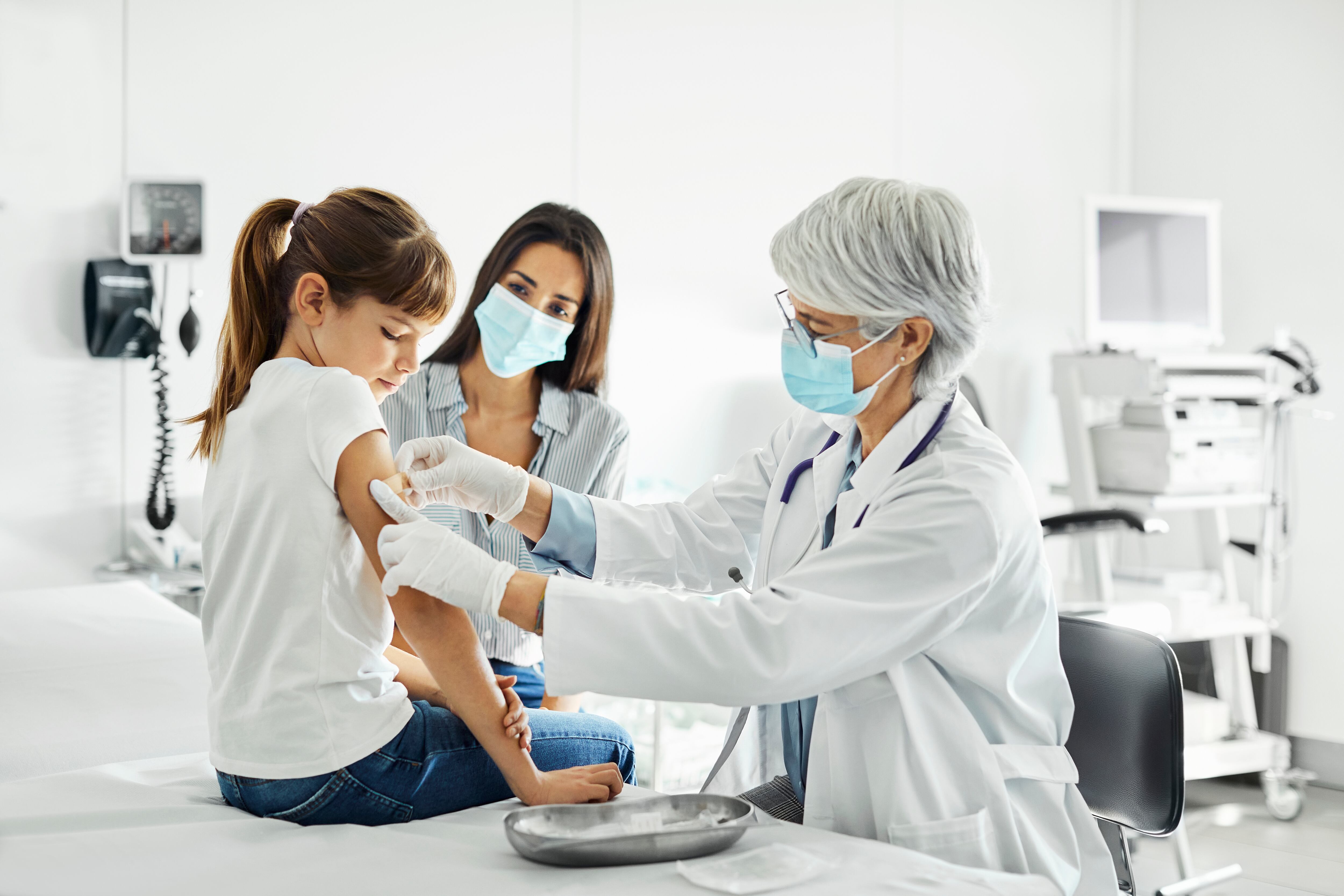 La pediatra está examinando al niño sentado en la mesa de examen. La familia está visitando la clínica durante el brote de COVID-19.