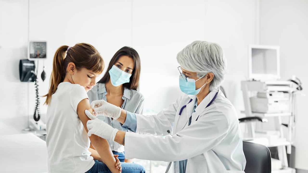La pediatra está examinando al niño sentado en la mesa de examen. La familia está visitando la clínica durante el brote de COVID-19.