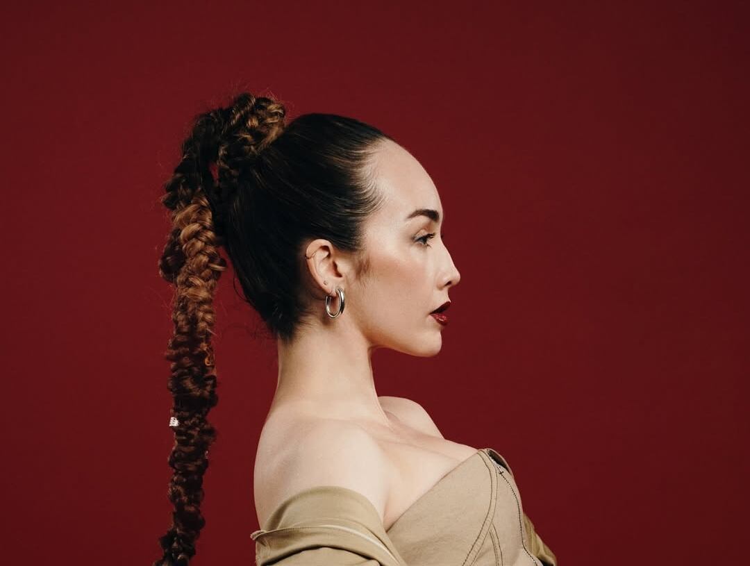 Ayiiti posando en un entorno urbano con vestimenta colorida, representando su identidad caribeña y su propuesta musical.