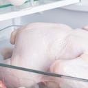 close-up of a whole chicken, against the background of a white refrigerator, in a glass substrate