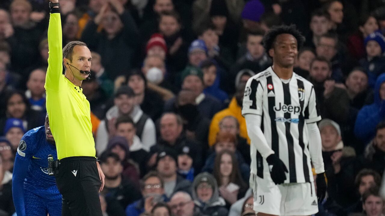Referee Srdjan Jovanovic, left, shows a yellow card to Juventus' Juan Cuadrado after he tackled Chelsea's Callum Hudson-Odoi during the Champions League group H soccer match between Chelsea and Juventus at Stamford Bridge stadium in London, Tuesday, Nov. 23, 2021. (AP Photo/Matt Dunham)