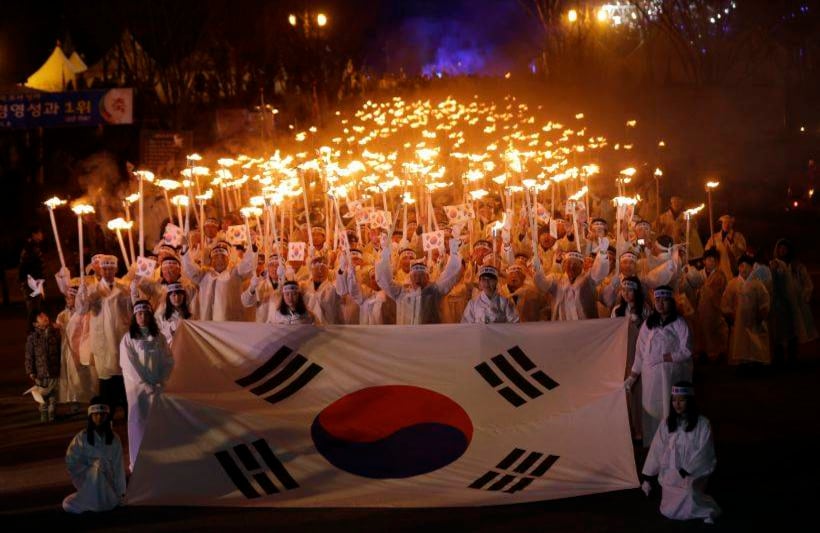 Surcoreanos, vestidos con trajes tradicionales, llevan antorchas y una gran bandera nacional mientras marchan en una calle durante una ceremonia de Independencia en 2013. FOTO:  Lee Jin-man/AP