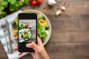 Blogger de comida usando un teléfono inteligente tomando fotos de una hermosa mezcla de ensalada verde fresca en una mesa de madera para compartir en las redes sociales
