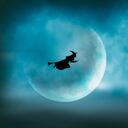 A witch flying on her broom across the sky is silhouetted in front of a large moon on Halloween night.