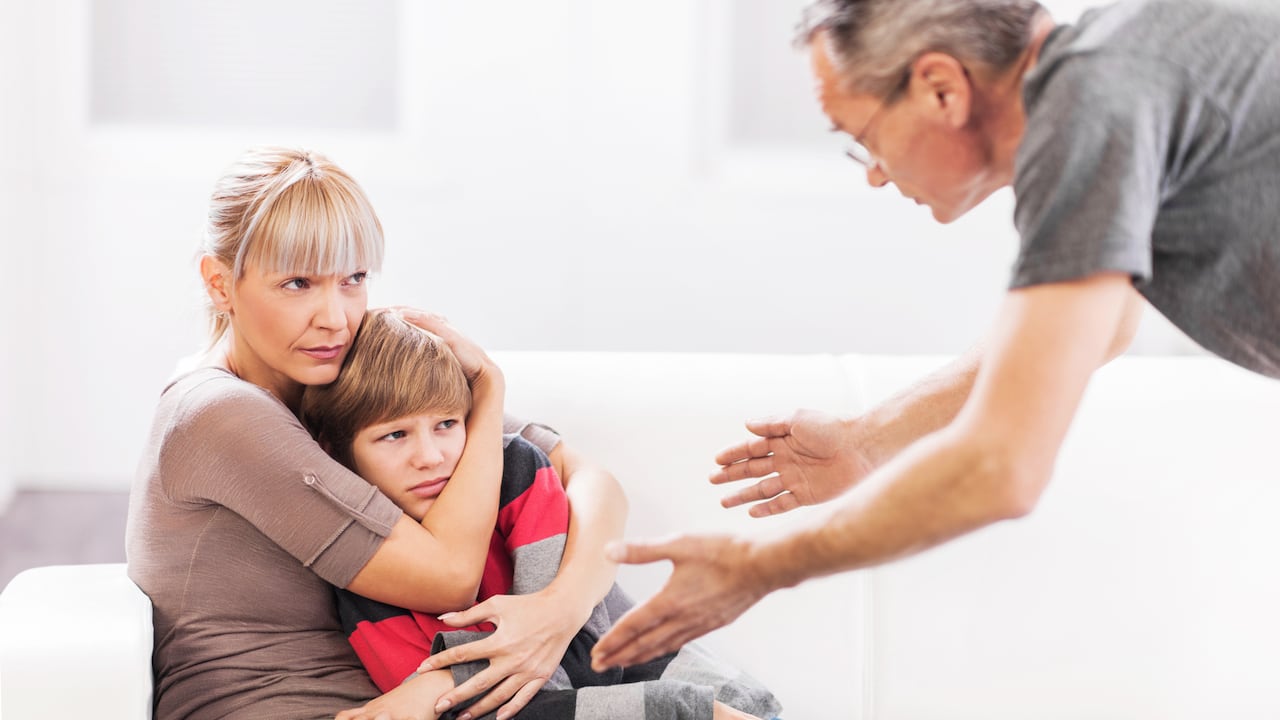 Mature father is scolding his son while mother is defending him.