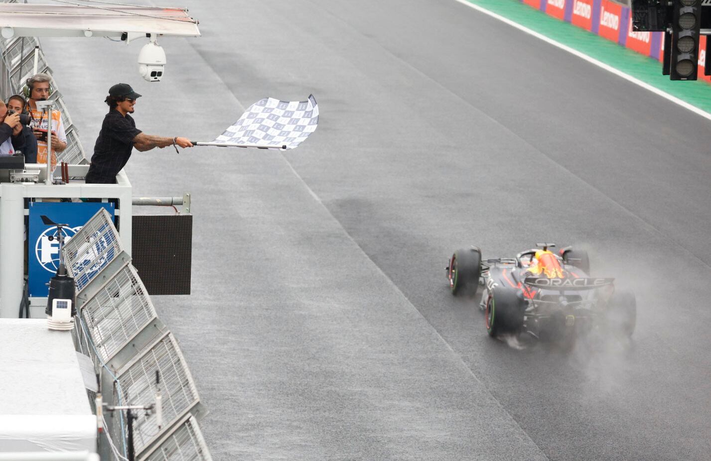 El piloto de Red Bull, Max Verstappen, de los Países Bajos, recibe la bandera a cuadros ondeada por el surfista brasileño Gabriel Medina para ganar el Gran Premio de Brasil de Fórmula 1 en la pista de carreras Interlagos en Sao Paulo, Brasil, el domingo 3 de noviembre de 2022. (Sebastian Moreira/Pool vía AP)