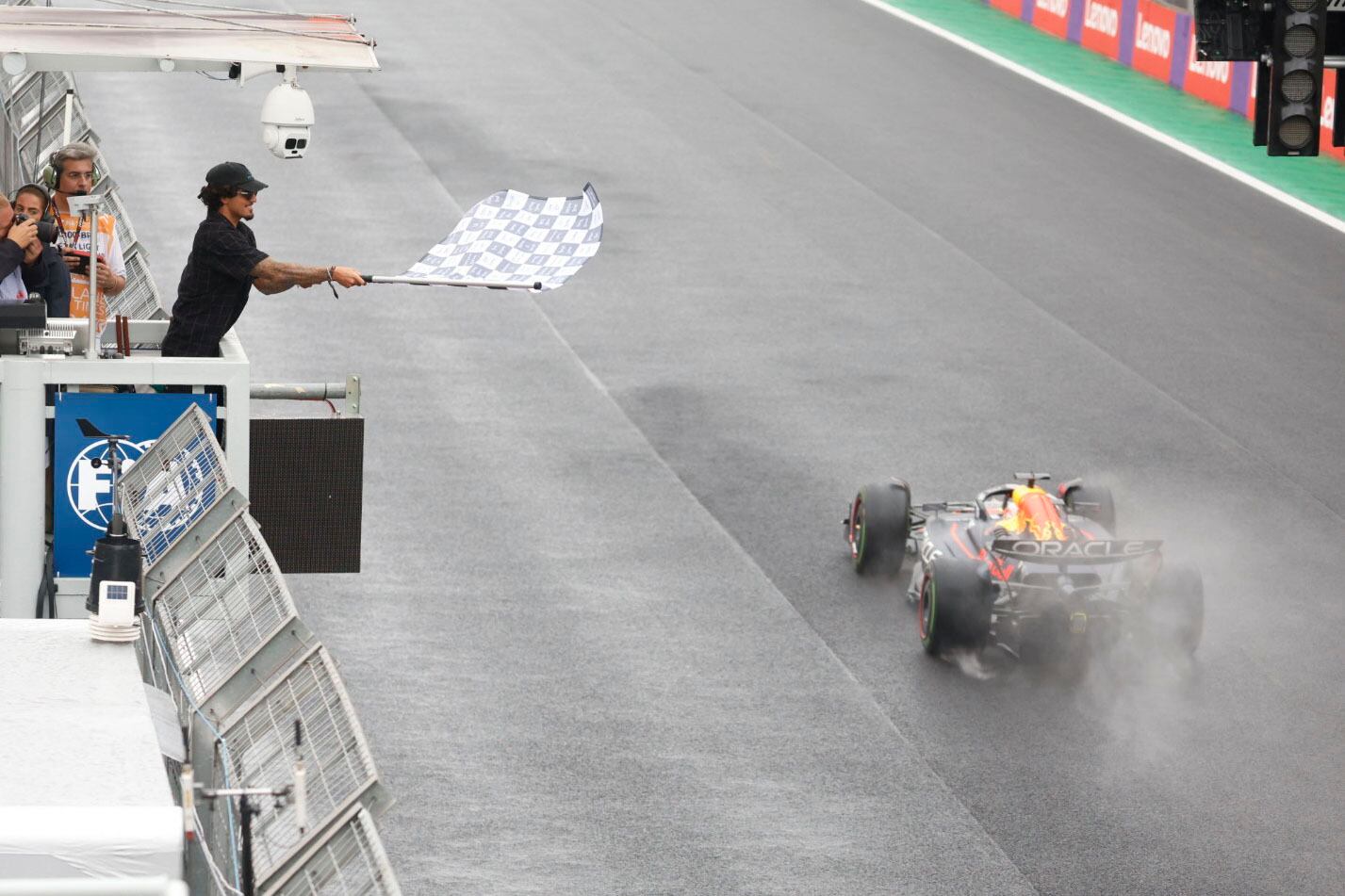 El piloto de Red Bull, Max Verstappen, de los Países Bajos, recibe la bandera a cuadros ondeada por el surfista brasileño Gabriel Medina para ganar el Gran Premio de Brasil de Fórmula 1 en la pista de carreras Interlagos en Sao Paulo, Brasil, el domingo 3 de noviembre de 2022. (Sebastian Moreira/Pool vía AP)