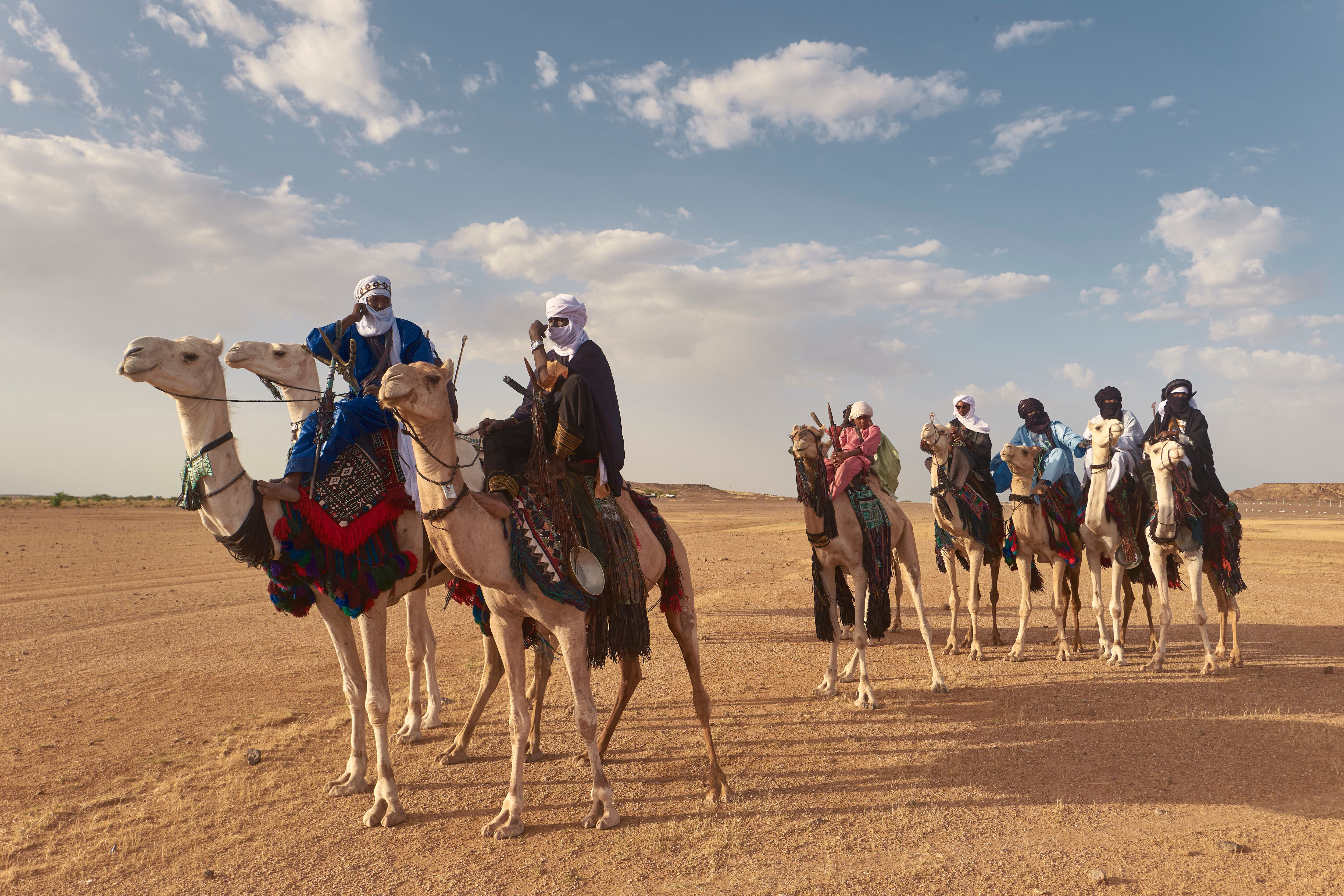 Men ride their camels during the annual festival for nomad people called Cure Salee in Ingall, in Niger on September 16, 2021. - Red, orange, blue, fuchsia ... For three days the Saharan desert of Ingall, in the north of Niger, was draped with the colors of the tunics of thousands of herders who came to celebrate their traditions. (Photo by Michele Cattani / AFP)