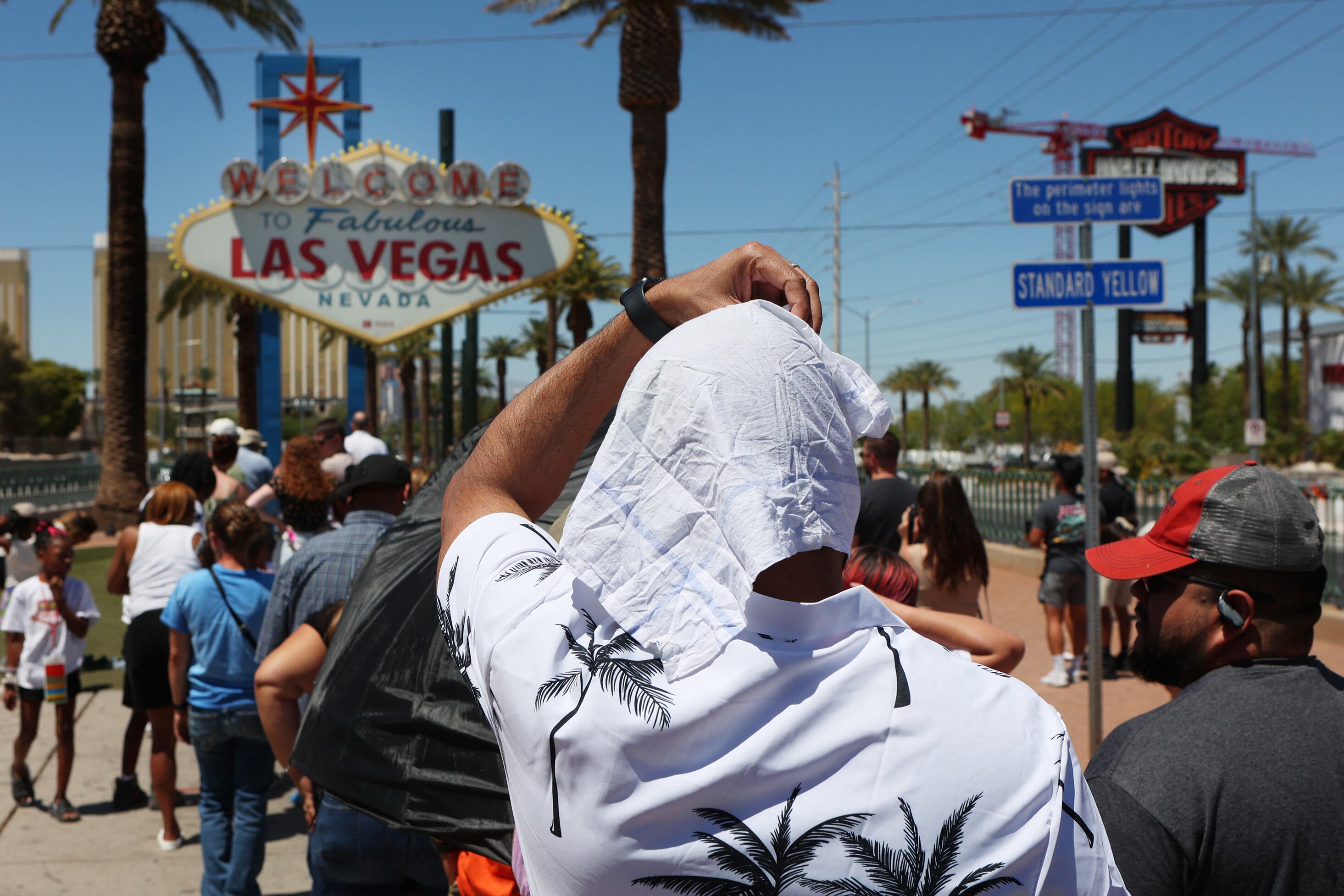 Hombre se protege del sol mientras espera en la fila para tomar una foto en el histórico cartel de Bienvenido a Las Vegas durante una ola de calor en Las Vegas, Nevada, el 14 de julio de 2023.