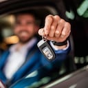 Photo of mid adult man sitting in new car and showing car keys. Focus on foreground.