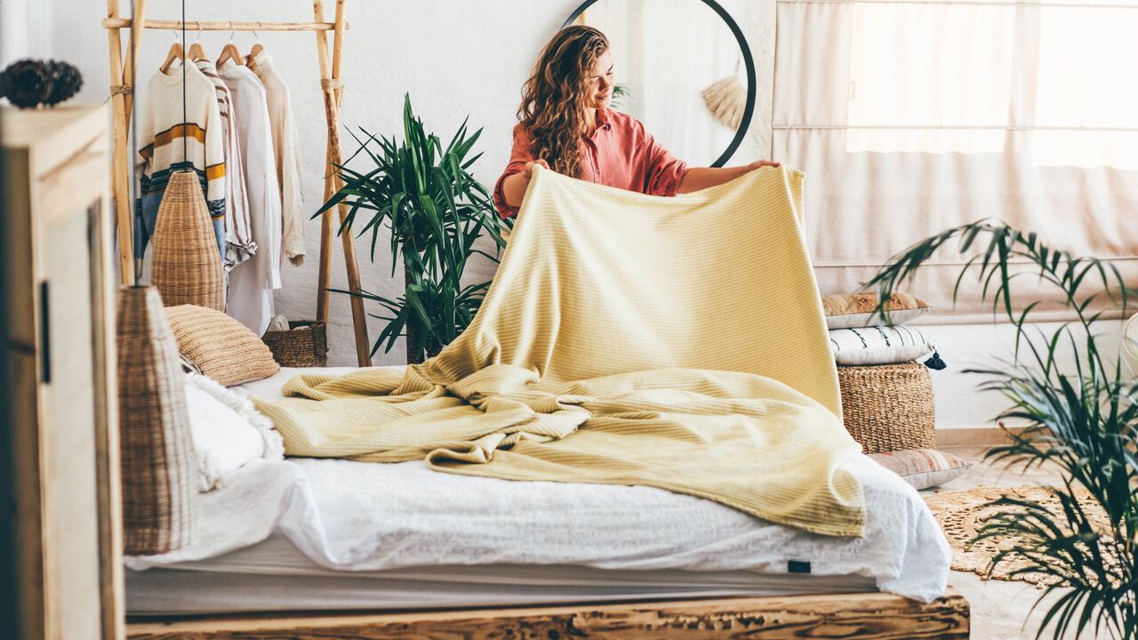 Woman doing her morning routine, arranging pillows and making up bed at home.