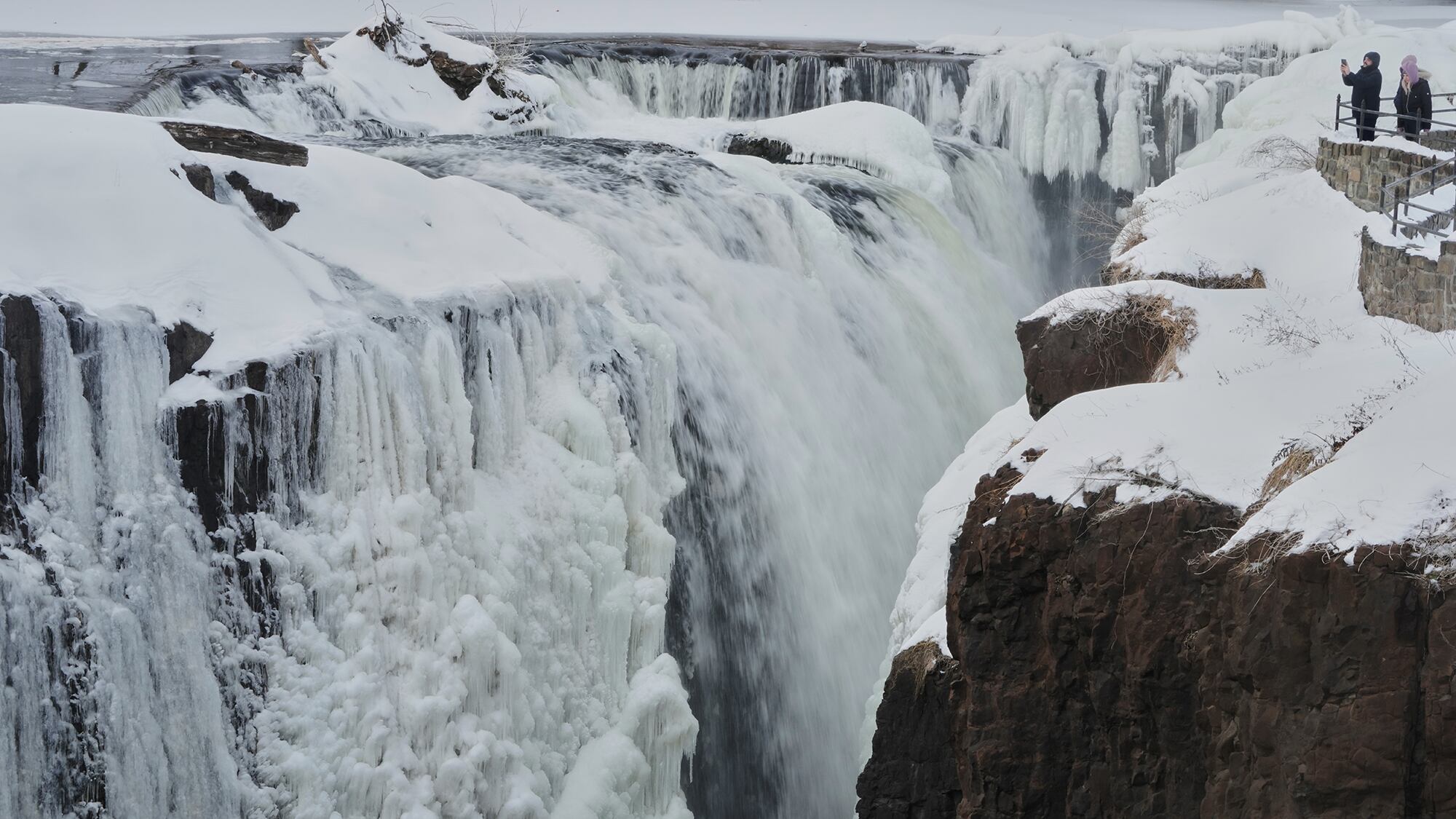 La gente mira las Great Falls parcialmente congeladas en Paterson, Estados Unidos. Miércoles 28 de enero de 2026.