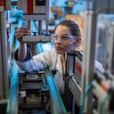 Ingeniero de sexo femenino que examina la pieza de la máquina en una línea de producción.