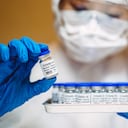 Healthcare professional in protective gloves & workwear holding & organising a tray of COVID-19 vaccine vials. The professional is carrying out researches on COVID-19 vaccine in laboratory.