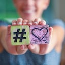 Mujer sosteniendo un signo de corazón de amor hashtag y sonriendo. Concepto de agrado de influencer en línea.
