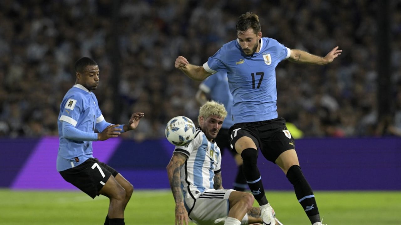 El mediocampista argentino Rodrigo De Paul (C) lucha por el balón con el mediocampista uruguayo Nicolás De La Cruz (L) y el defensor Matías Viña (R) durante el partido de fútbol clasificatorio suramericano para la Copa Mundial de la FIFA 2026 entre Argentina y Uruguay en el estadio La Bombonera de Buenos Aires. Aires el 16 de noviembre de 2023. (Foto de JUAN MABROMATA/AFP)