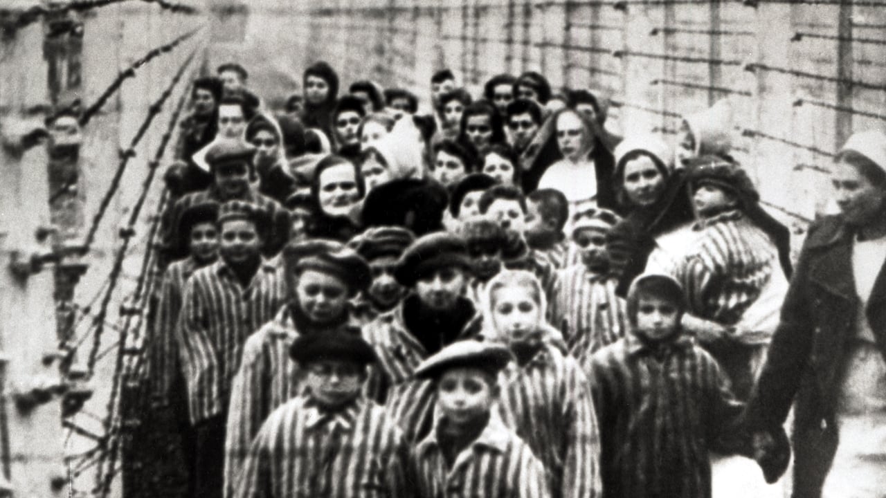 Niños judíos, sobrevivientes de Auschwitz, con una enfermera detrás de una cerca de alambre de púas, Polonia, febrero de 1945. Foto tomada por un fotógrafo ruso durante la realización de una película sobre la liberación del campo. Los niños fueron vestidos por los rusos con ropa de prisioneros adultos. (Foto de Galerie Bilderwelt/Getty Images)