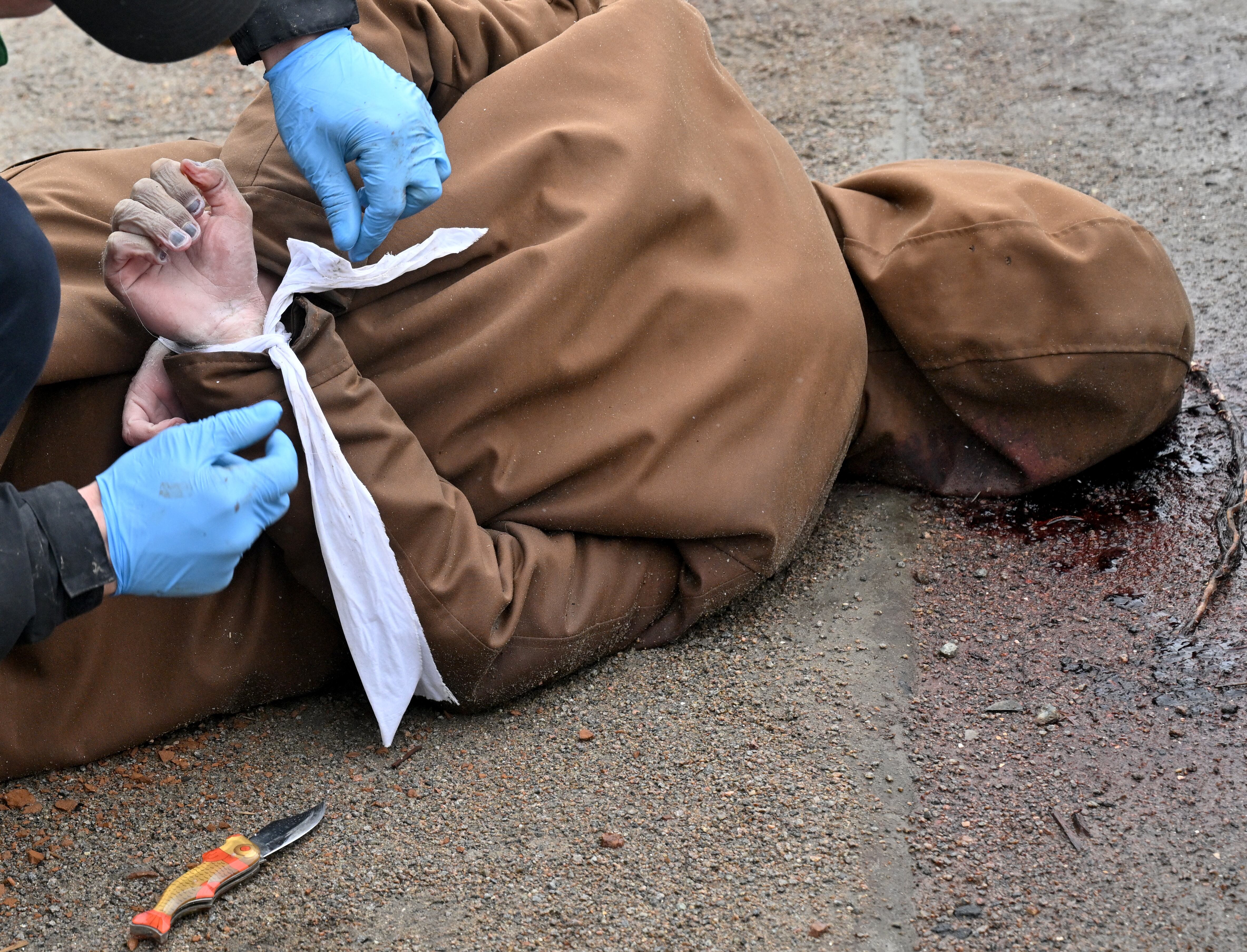 Contenido gráfico / Un trabajador comunal libera las muñecas de un hombre muerto, con las manos atadas a la espalda, en la ciudad de Bucha, no lejos de la capital ucraniana, Kiev, el 3 de abril de 2022. - El presidente Volodymyr Zelensky acusó a Rusia de cometer genocidio e intentar eliminar a "toda la nación" de Ucrania, un día después del descubrimiento de fosas comunes y civiles aparentemente ejecutados cerca de Kiev. Ucrania recuperó 410 cuerpos de civiles de áreas que recientemente recuperó del ejército ruso en la región más amplia de Kiev, dijo el domingo su fiscal general Iryna Venediktova. (Photo by Sergei SUPINSKY / AFP)