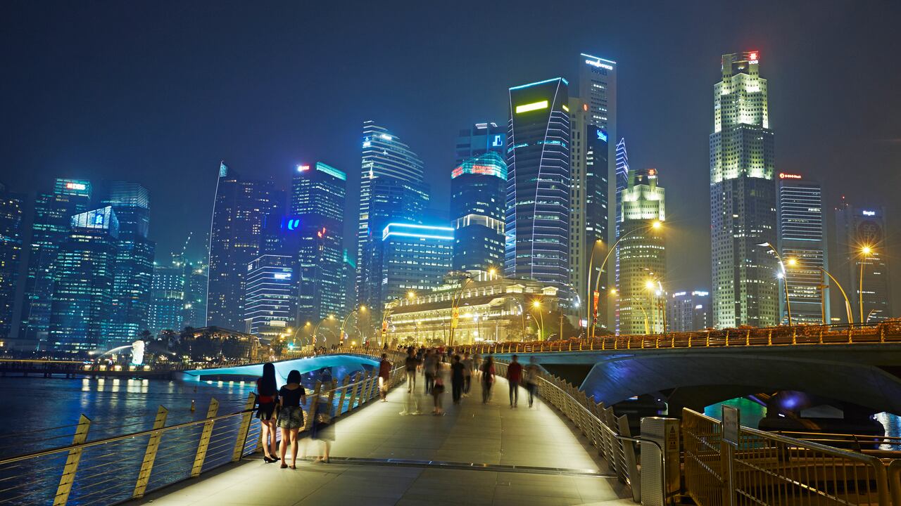 Línea de rascacielos en el distrito financiero de Singapur y Marina Bay iluminada por la noche.