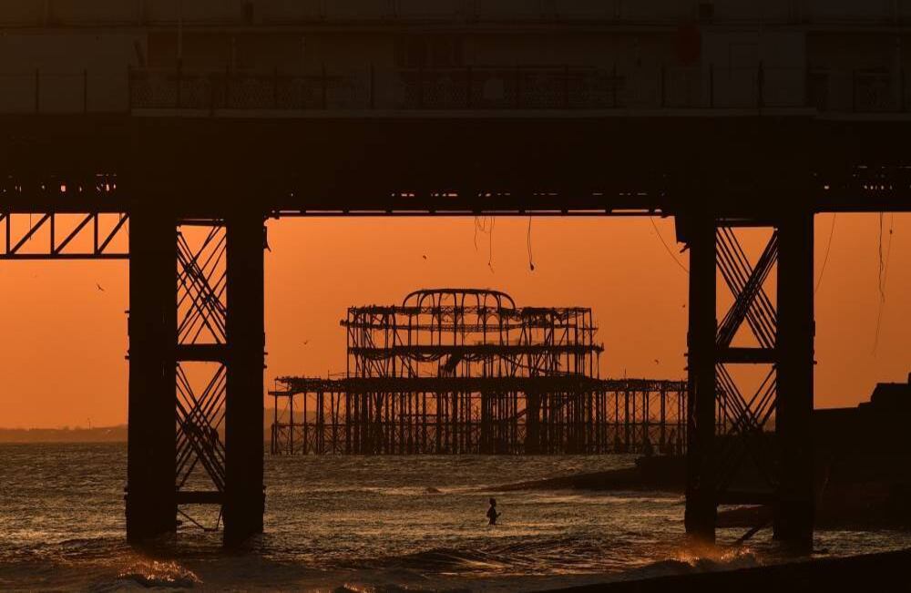 Un bañista se da un chapuzón cuando el sol se pone detrás del abandonado muella West Pier en Brighton, en la costa sur de Inglaterra. Hasta 1,5 millones de personas vulnerables en Gran Bretaña, identificadas como las más expuestas a la epidemia de coronavirus, deberían quedarse en casa por al menos 12 semanas, dijo el gobierno este domingo, 22 de marzo. Foto: Glyn Kirk / AFP