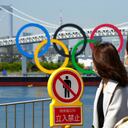 Women walk by a "no trespassing" sign at a park with a backdrop of the Olympic rings floating in the water in the Odaiba section Thursday, March 18, 2021, in Tokyo. Tokyo Olympics creative director Hiroshi Sasaki is resigning after making demeaning comments about Naomi Watanabe, a well-known female celebrity. Sasaki who was in charge of the opening and closing ceremonies for the Olympics, told planning staff members last year that Watanabe could perform in the ceremony as an “Olympig.” (AP Photo/Eugene Hoshiko)