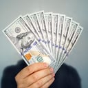 Manos sosteniendo dólares en efectivo. 1000 dólares en 100 billetes en el primer plano de la mano de un hombre sobre un fondo oscuro.