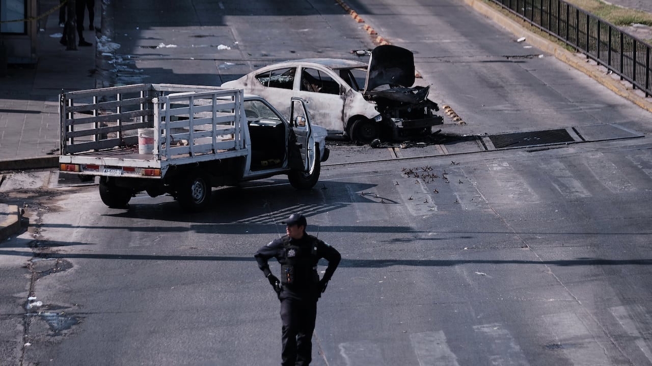 Un policía vigila un vehículo calcinado tras ser incendiado en una carretera de Guadalajara, tras la muerte del líder del cártel Jalisco Nueva Generación, El Mencho.
