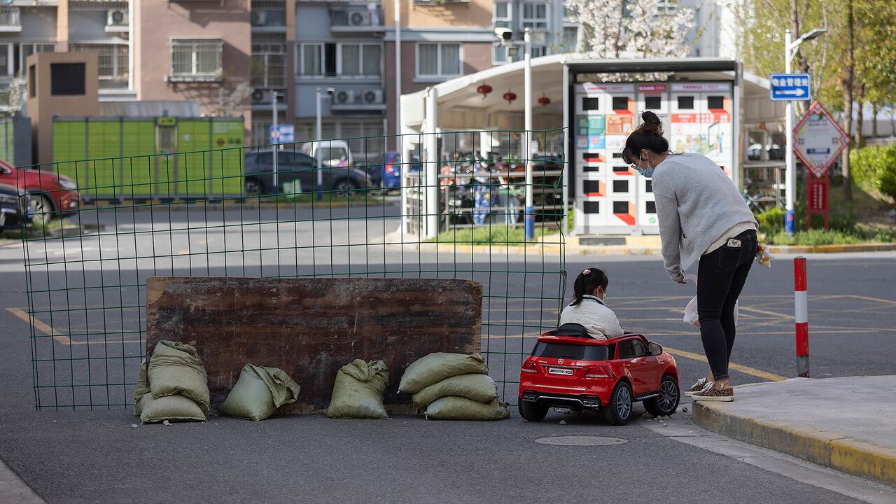 Una madre observa a su hija jugar en un coche de juguete junto a una barrera instalada en la puerta de una comunidad residencial bajo encierro en Shanghái, China