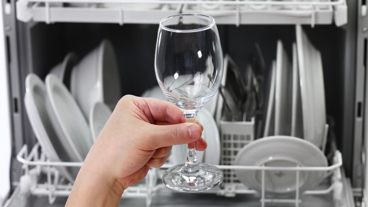 dishwasher, open and loaded with dishes, man hand taking out clean wine glass, after washing
