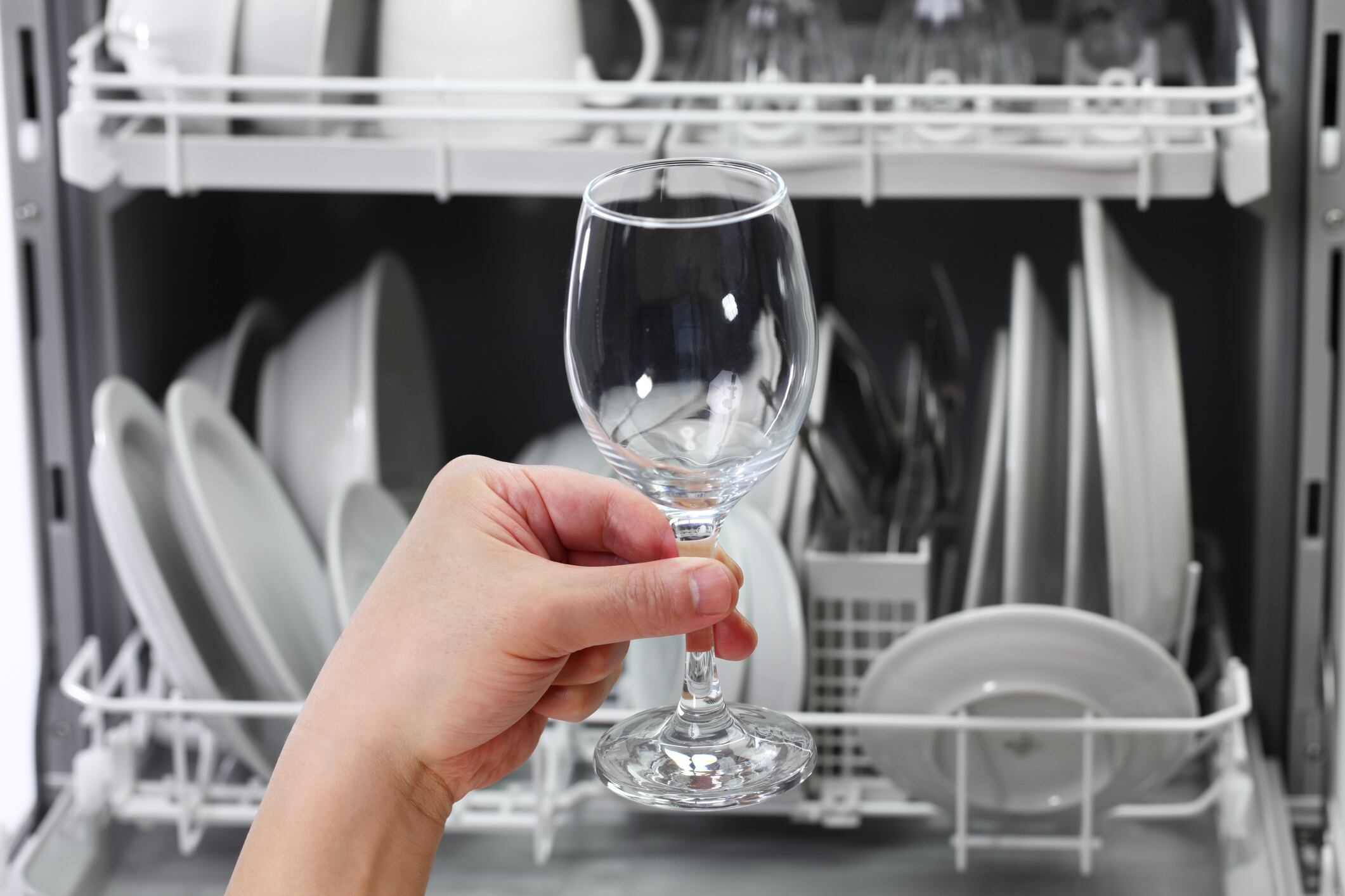 dishwasher, open and loaded with dishes, man hand taking out clean wine glass, after washing