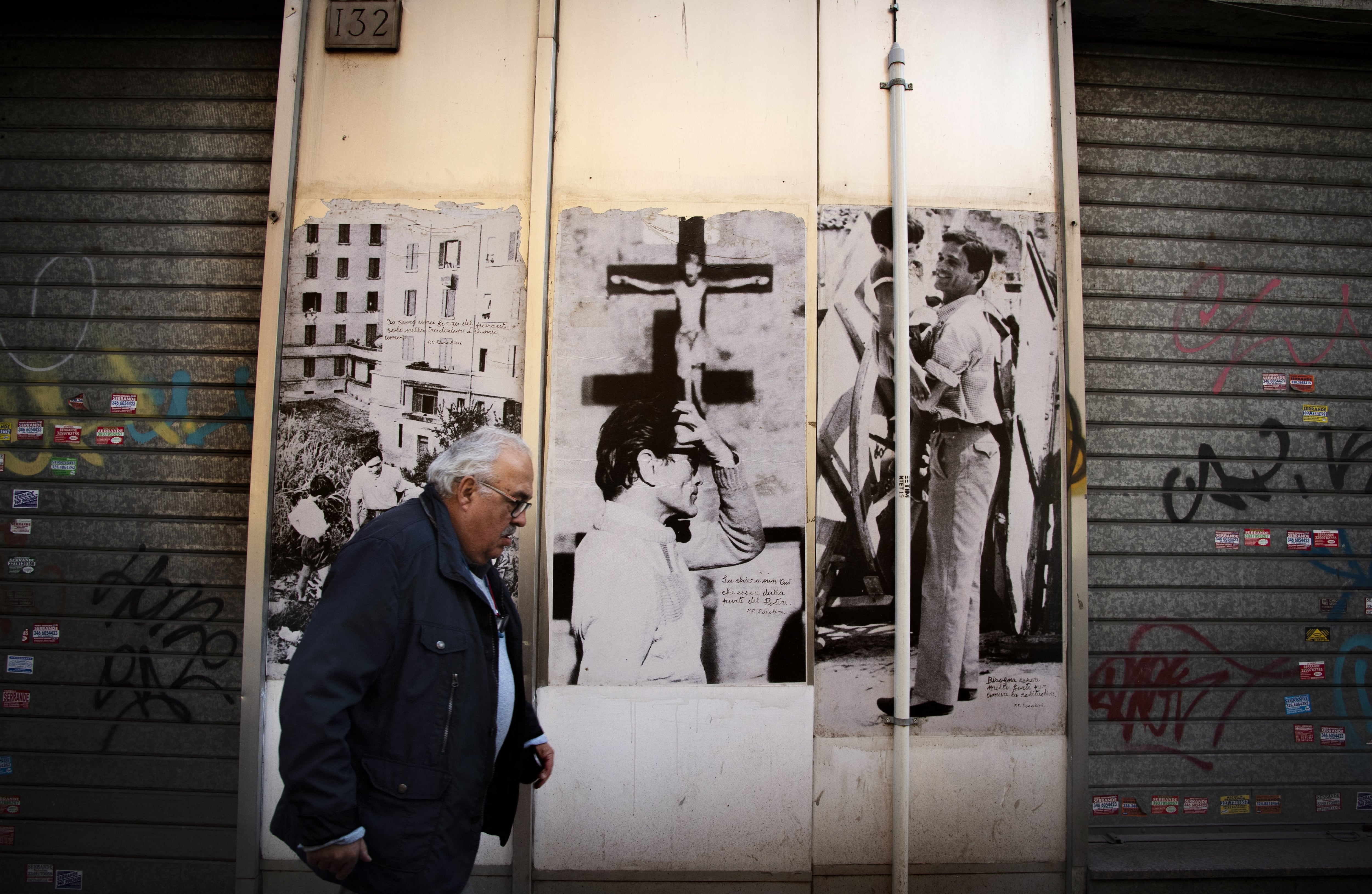 EA man passes by Pasolini's pictures on the wall of the worlshop of Silvio Parrello, dubbed "Er Pecetto", in Monteverde district in Rome, on February 16, 2022. - Between photos, press clippings, paintings, rare books and above all memorabilia, Er Pecetto, 79, the son of a shoemaker, is considered in Rome as the guardian of the memory of the poet, writer and filmmaker Pier Paolo Pasolini, who would fulfill 100 years on March 5, 2022. Foto: Tiziana FABI / AFP.
