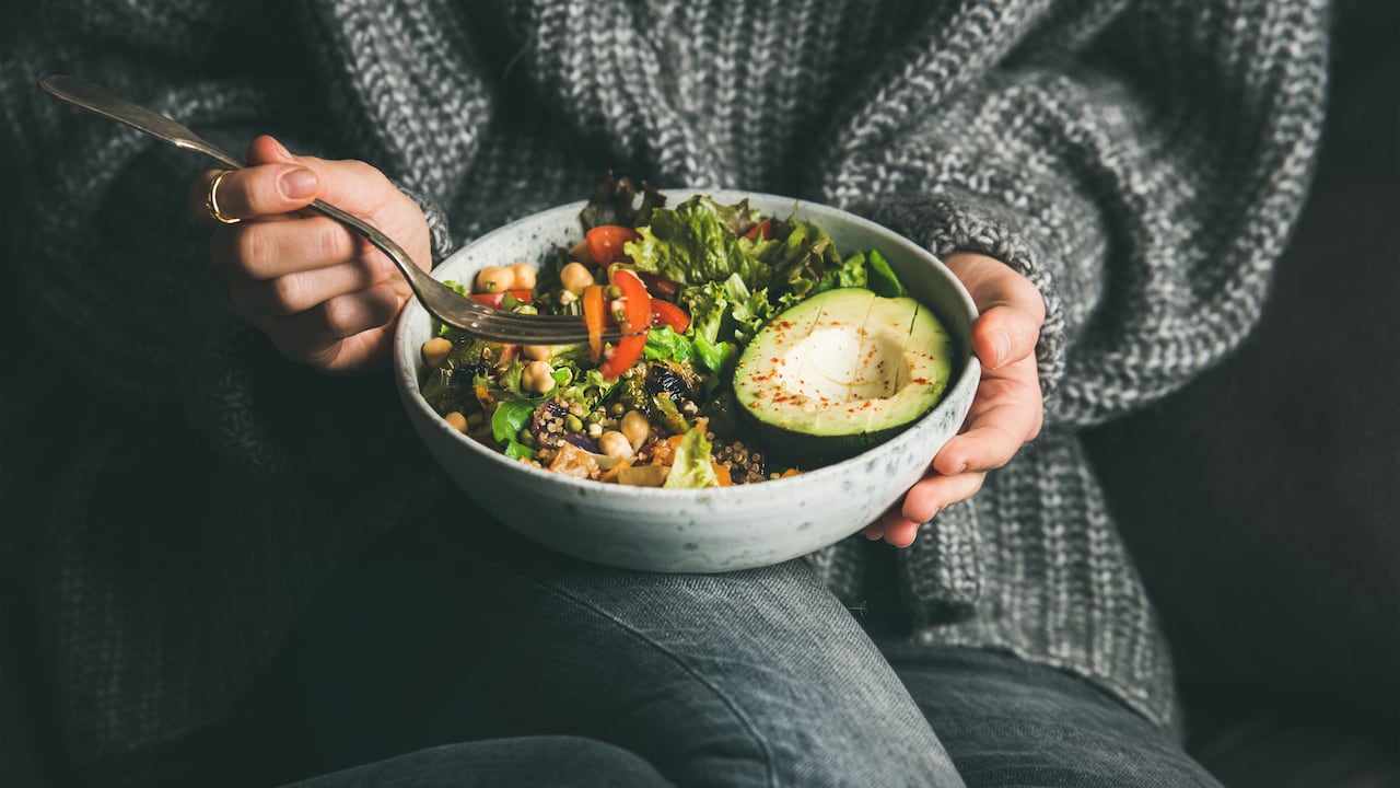 Woman in sweater eating fresh salad, avocado, beans and vegetables