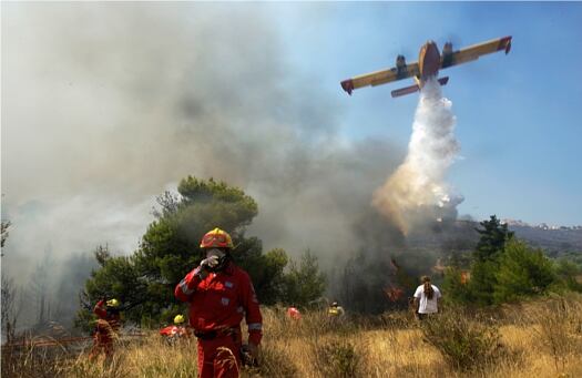 Aviones riegan agua sobre el bosque ardiente en Dioni, al este de Atenas, Grecia. Los vientos de más de 60 kilómetros por momentos han impedido el despegue de las 12 aeronaves disponibles para sobrevolar la zona y sofocar las llamas que avanzan rápidamente.