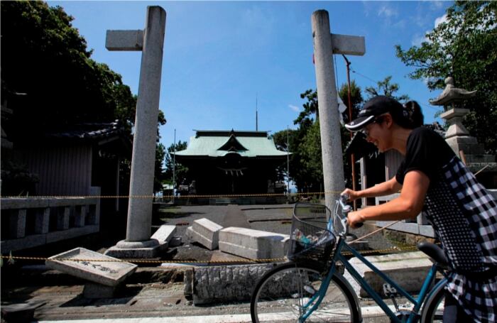 Una mujer empuja su bicicleta delante de una puerta de piedra dañada en una capilla sintoísta en Yaizu, en Shizuoka, Japón. 