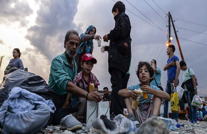 Los migrantes comen mientras esperan el permiso para salir del campo de registro y subir a un autobús con destino a Serbia.