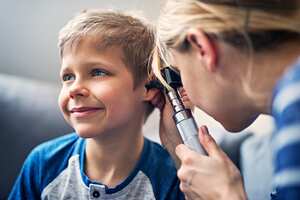 Little boy having a medical ear examination. The smiling boy is aged 7. The doctor is vising boy at home and using otoscope to examine the boy's ear.
