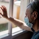 Un abuelo tocando la ventana interior y su nieto tocando la ventana desde el exterior. Ambos con mascarillas.