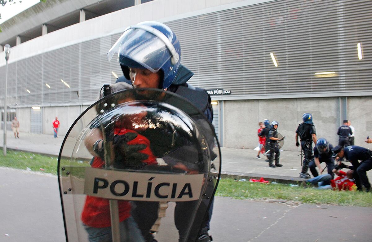 Un policía antidisturbios sostiene un niño que llora al ver que su padre es atacado con bastones por los otros agentes, como se evidencia en la parte derecha, fuera de un estadio en Guimarães, Portugal. (AP/Delfim Machado)