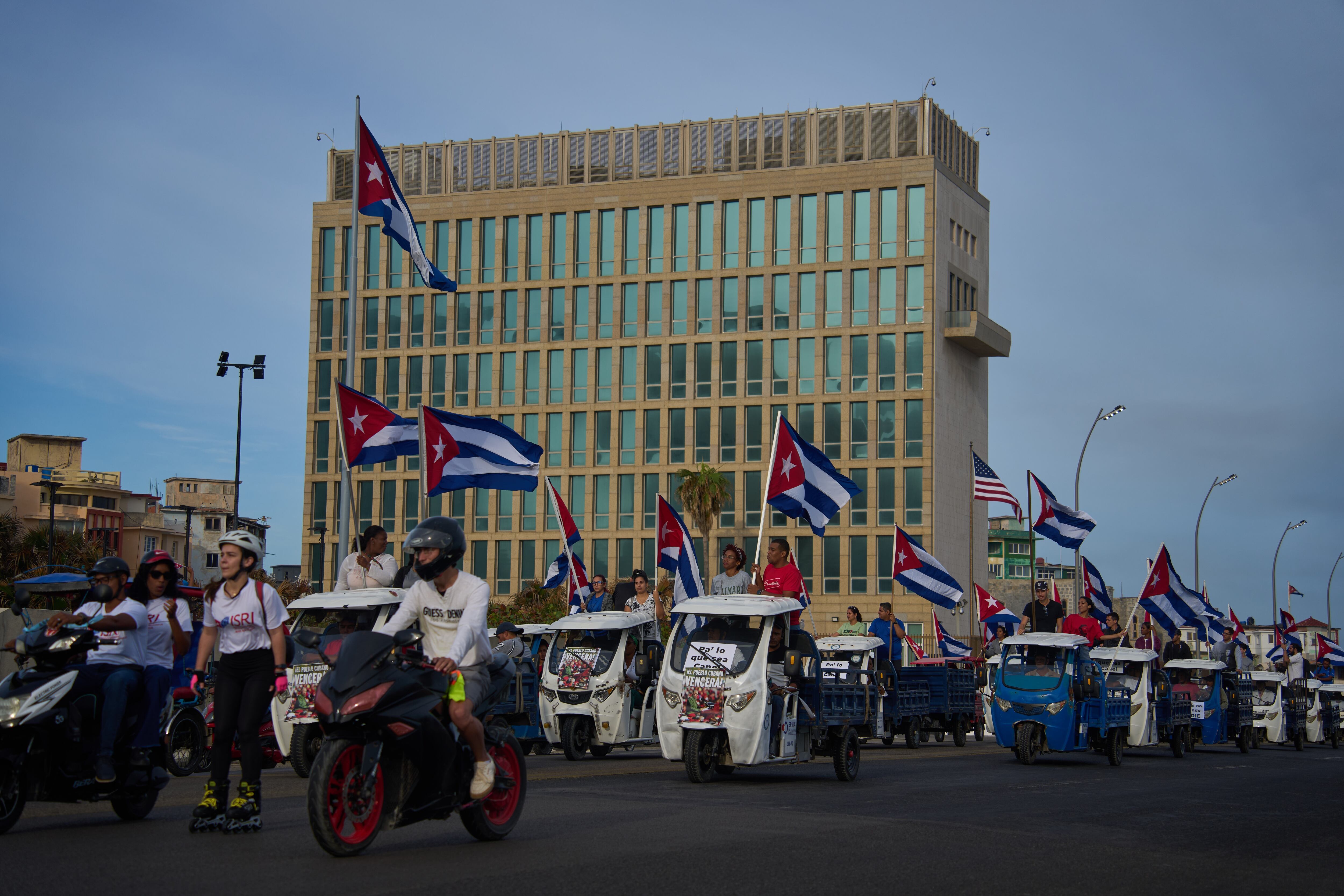 Varias personas pasan en vehículos eléctricos frente a la embajada de Estados Unidos durante una marcha juvenil antiimperialista organizada por el gobierno en La Habana, Cuba.