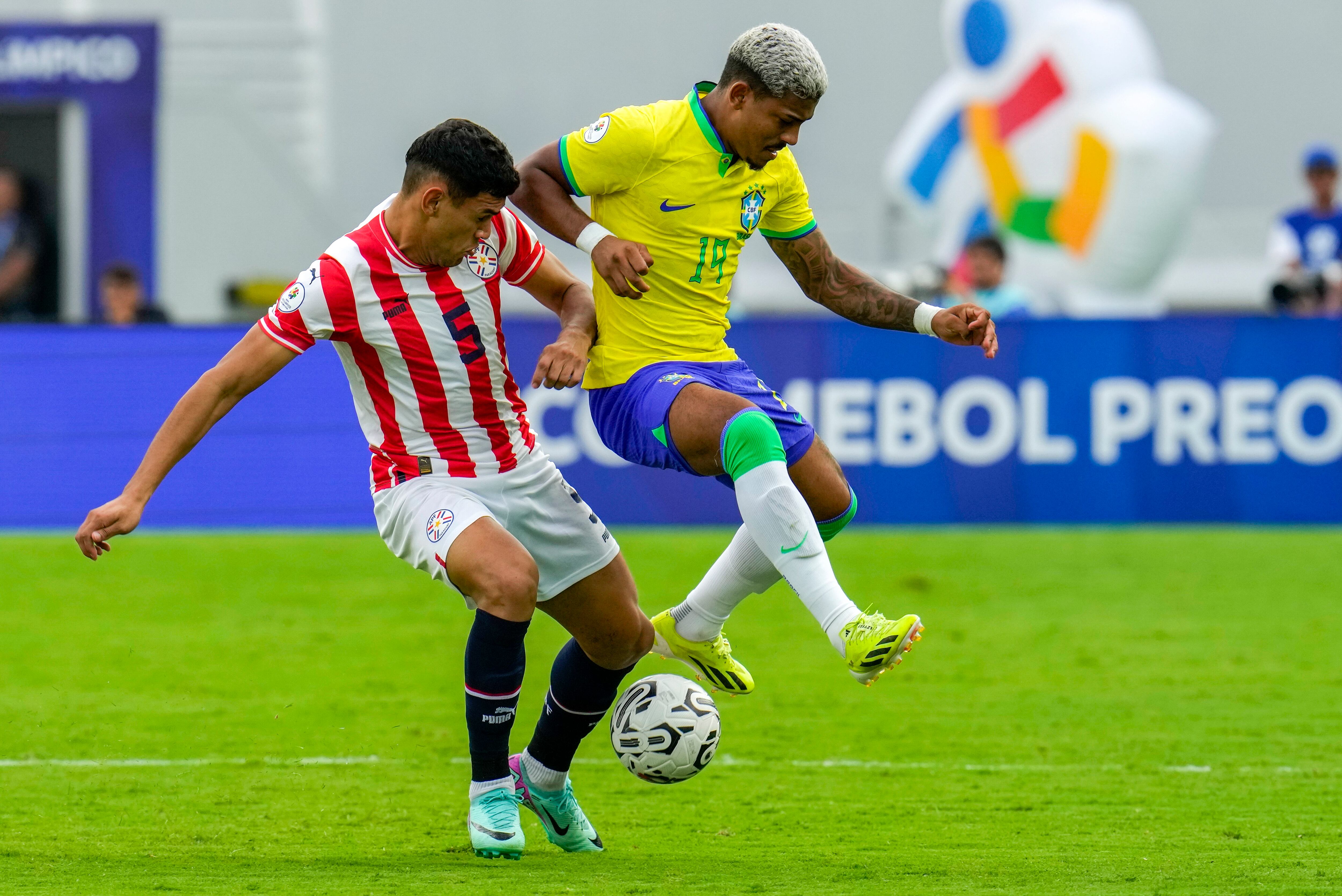 El paraguayo Gilberto Flores, izquierda, y el brasileño John Kennedy luchan por el balón durante el partido de fútbol del torneo preolímpico sudamericano sub-23 en el estadio Brígido Iriarte en Caracas, Venezuela, el lunes 5 de febrero de 2024. (Foto AP/Ariana Cubillos)