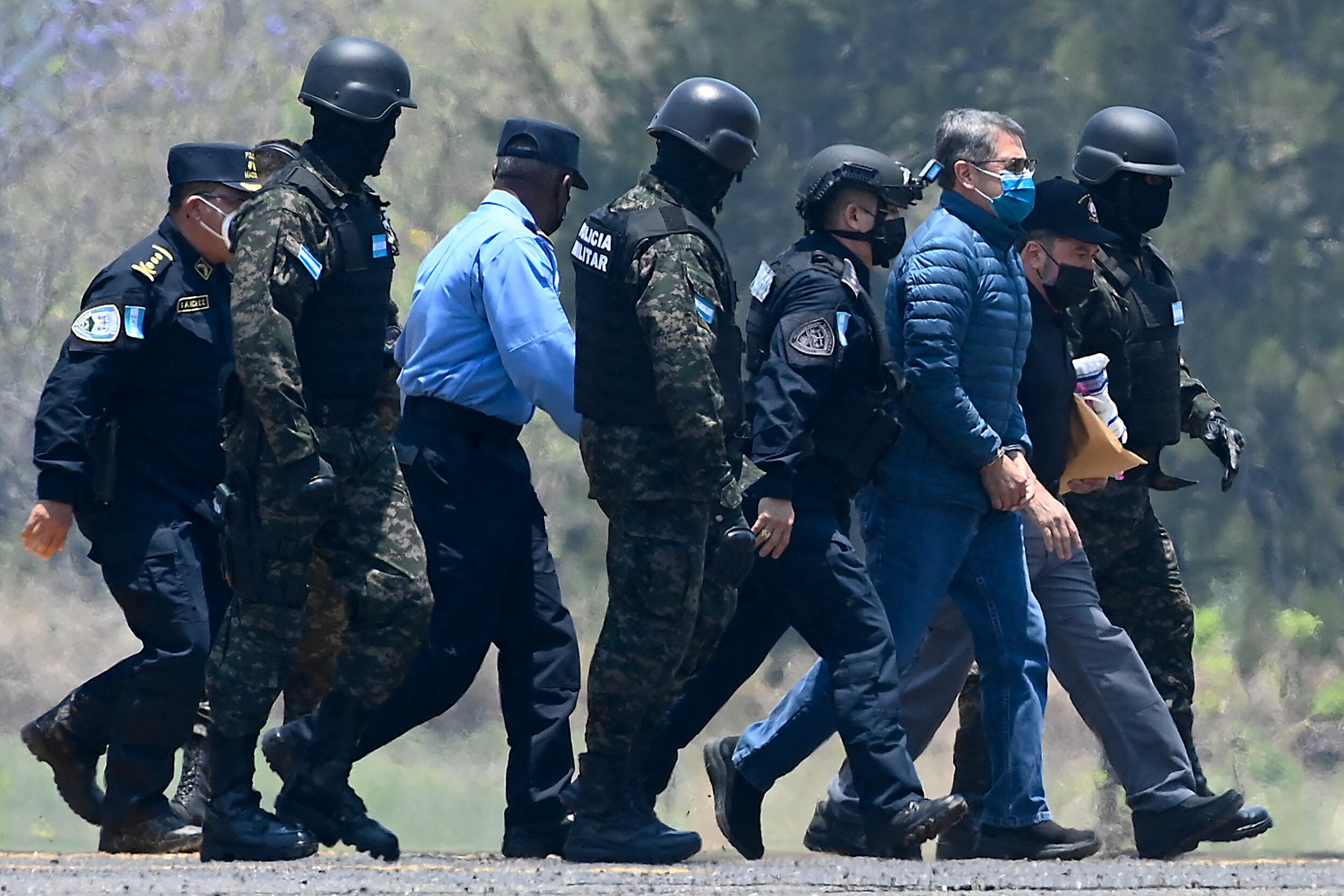 El expresidente de Honduras Juan Orlando Hernández (3-R) fue escoltado por agentes policiales a su llegada a una base de la Fuerza Aérea en Tegucigalpa, el 21 de abril de 2022, antes de ser extraditado a Estados Unidos para enfrentar cargos relacionados con el narcotráfico. (Foto por Orlando SIERRA / AFP)