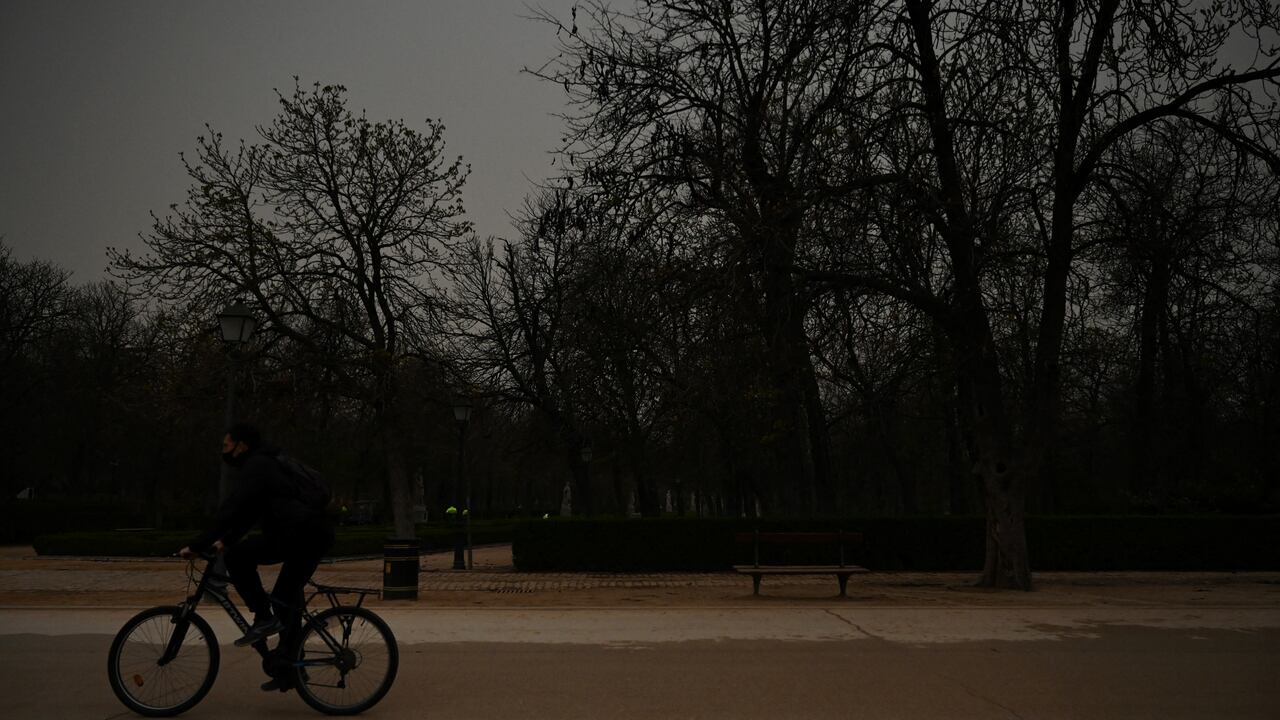 Un ciclista monta su bicicleta mientras la arena del Sahara que cayó durante la noche cubre la carretera en el parque del Retiro en Madrid el 15 de marzo de 2022. - Este fenómeno meteorológico, fuertes vientos calientes cargados de polvo de arena del desierto del Sahara, se llama en España el "calima".