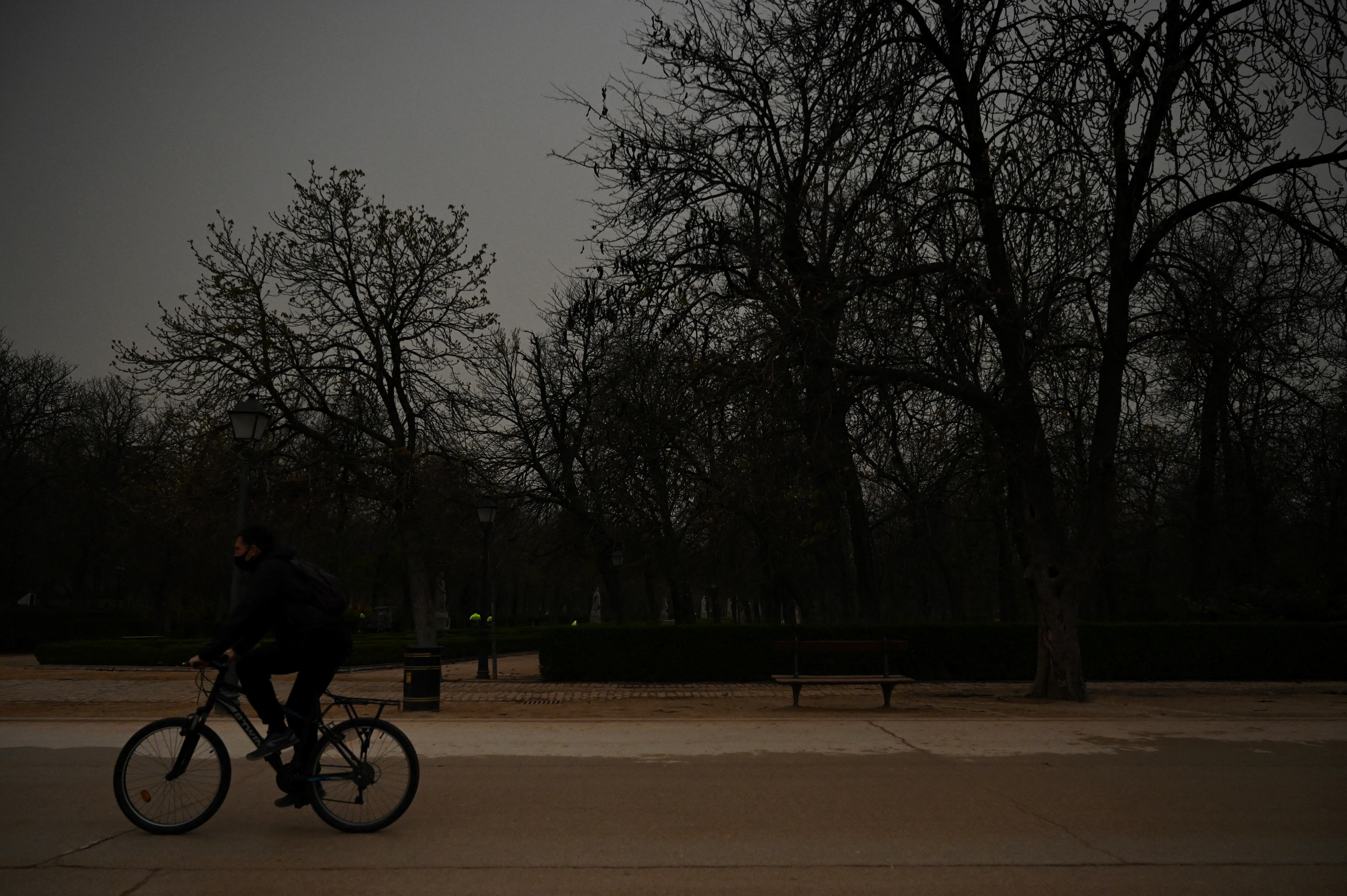Un ciclista monta su bicicleta mientras la arena del Sahara que cayó durante la noche cubre la carretera en el parque del Retiro en Madrid el 15 de marzo de 2022. - Este fenómeno meteorológico, fuertes vientos calientes cargados de polvo de arena del desierto del Sahara, se llama en España el "calima".