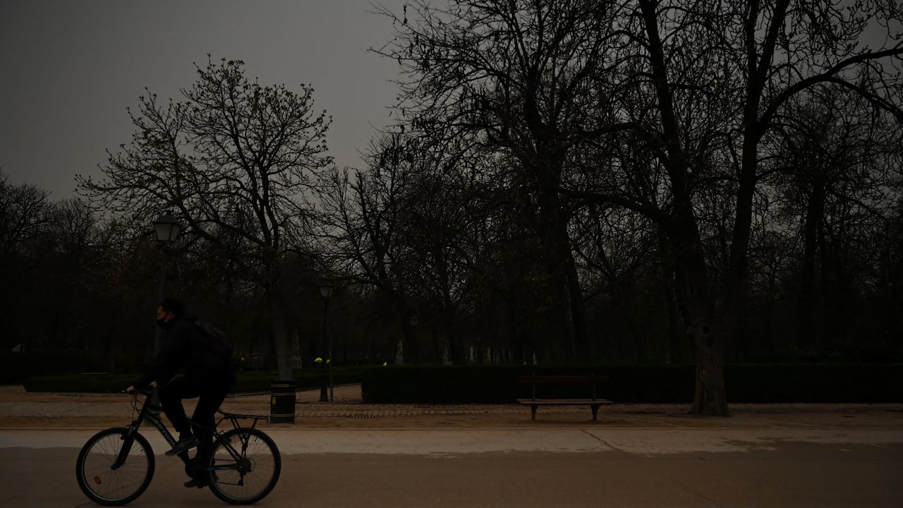 Un ciclista monta su bicicleta mientras la arena del Sahara que cayó durante la noche cubre la carretera en el parque del Retiro en Madrid el 15 de marzo de 2022. - Este fenómeno meteorológico, fuertes vientos calientes cargados de polvo de arena del desierto del Sahara, se llama en España el "calima".(Photo by Gabriel BOUYS / AFP)