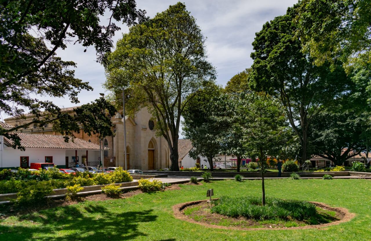 Durante la Colonia la plaza principal de Tenjo era el lugar donde se reunían los indios para su adoctrinamiento, convirtiéndose en un escenario con particularidades únicas, en comparación con las demás plazas de la sabana. Fue declarada monumento nacional el 17 de diciembre de 1993, junto con los predios y construcciones de las cuatro esquinas que conforman la plaza. A su alrededor está la Iglesia Santiago Apóstol, construida en 1603, año en que empezó la historia del municipio. Foto: Alcaldia Tenjo