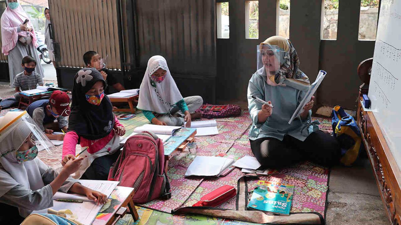 La maestra Inggit Andini, a la derecha, dicta clases a sus alumnos con un protector facial en un aula improvisada en su residencia de Tangerang, Indonesia, el lunes 10 de agosto. Andini ofreció lecciones adicionales gratuitas para los estudiantes que carecen de acceso a Internet, ya que la escuela en la que trabaja permanece cerrada e implementó las clases virtuales. Foto: Tatan Syuflana / AP